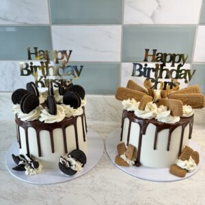 Two celebration cakes with white frosting and chocolate drip, topped with "Happy Birthday" toppers and cookies on each cake (oreo on left, biscuits on right).