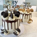 Cake topped with chocolate drip, white frosting rosettes, and Oreo cookies under a 'Happy Birthday' topper; two tiered festive cake with cookies and cookies-and-cream decorations.