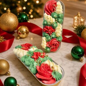 Decorative Christmas cookies piped in red, green, and white frosting in two metal tins on a marble table, with gold ornaments and red ribbon in the background.