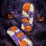 Two elongated trays of orange, purple, and white frosted cupcakes in a Halloween scene with jack-o'-lanterns, bats, and a full moon.