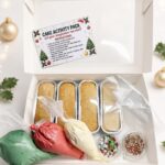 Open white gift box showing a Cake Activity Pack with four rectangular bake pans, piping bags in green, red, and white, plus sprinkle jars.
