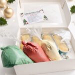 Open white box revealing a Christmas cake activity pack with three colored frosting bags (green, red, white) and decorating items inside.